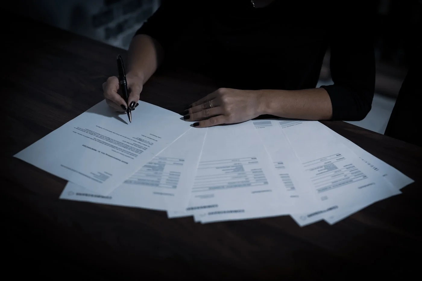 Hands carefully reviewing a fan of paperwork on a desk
