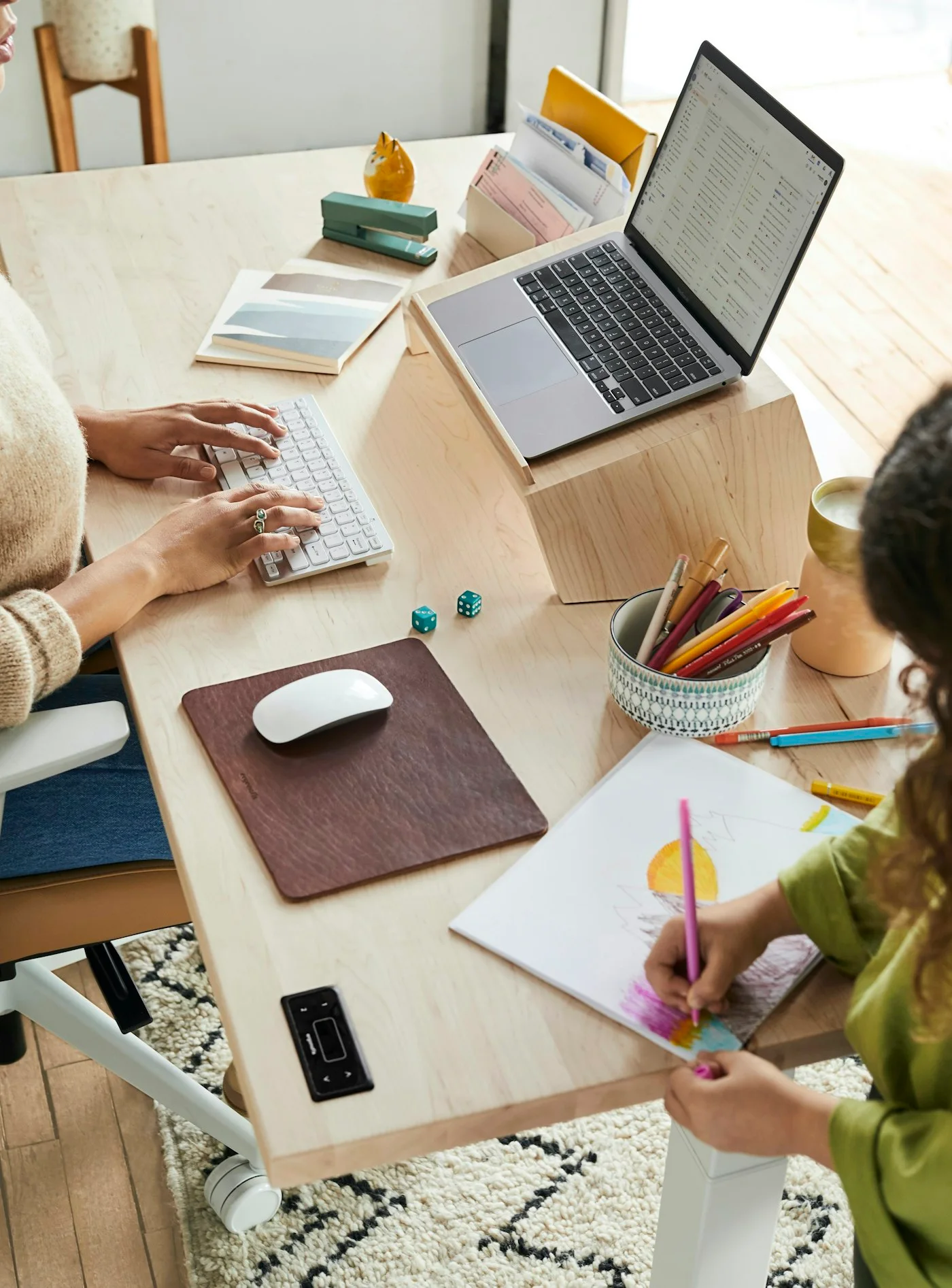 A mother working at her desk while her daughter draws beside her