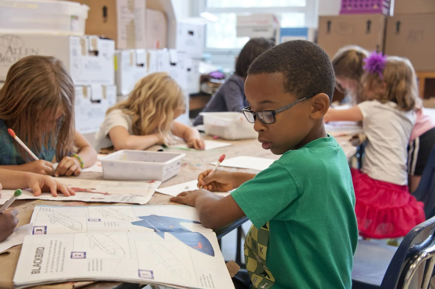 A focused young student working at his desk surrounded by classmates